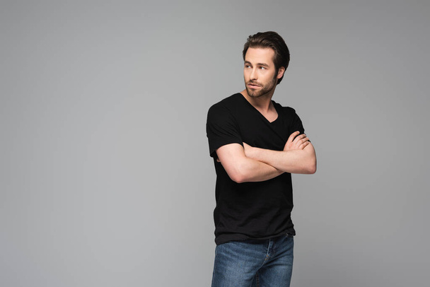 young bearded man in black t-shirt posing with crossed arms isolated on gray - Fotó, kép