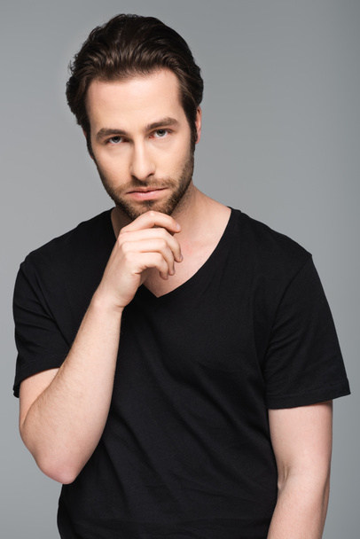 pensive man in black t-shirt looking at camera while posing isolated on gray - Foto, afbeelding