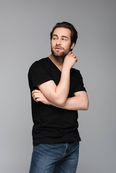 bearded and good-looking man in t-shirt looking away while posing isolated on gray - Foto, Bild