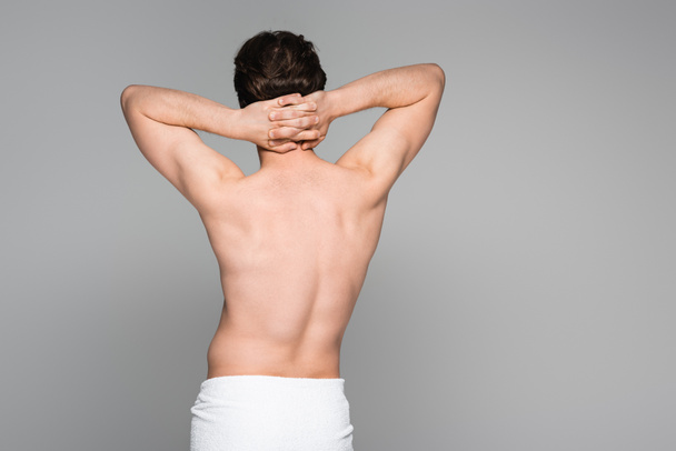 back view of shirtless man wrapped in towel standing with hands on neck isolated on grey  - Foto, afbeelding