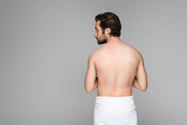 Muž bez košile zabalený v ručníku stojí a dívá se stranou izolované na šedé  - Fotografie, Obrázek