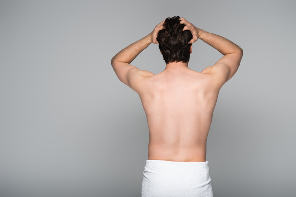 back view of shirtless man wrapped in towel adjusting hair isolated on grey  - Foto, Imagen