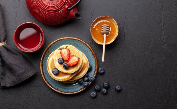 Gezond ontbijt met pannenkoeken en kruidenthee. Zelfgemaakte Amerikaanse pannenkoeken met bessen en honing. Bovenaanzicht plat lag met kopieerruimte - Foto, afbeelding