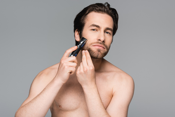 uomo senza maglietta con barba utilizzando rasoio elettrico isolato su grigio - Foto, immagini