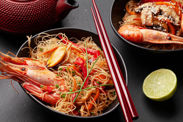 Wok with stir fried noodles, shrimps and vegetables on stone background - Photo, Image