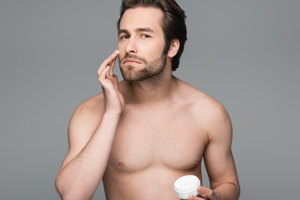 shirtless man applying moisturizing face cream isolated on grey  - Fotó, kép