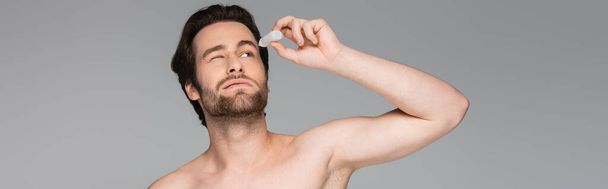 shirtless man with closed eye applying eye drops isolated on grey, banner - Foto, Bild