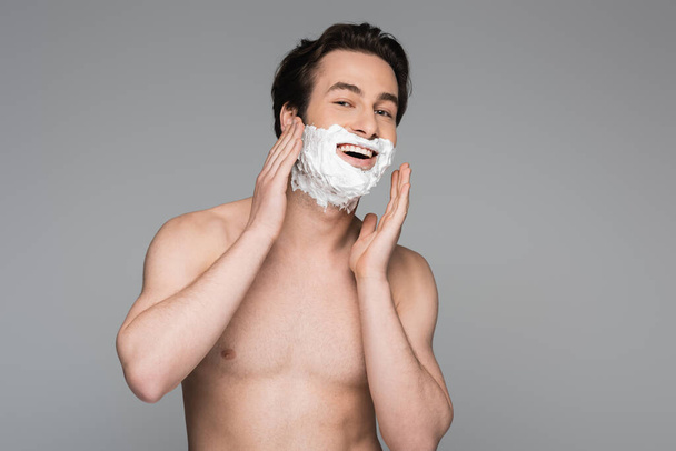 šťastný a bez košile muž s bílou pěnou holení obličeje izolované na šedé - Fotografie, Obrázek