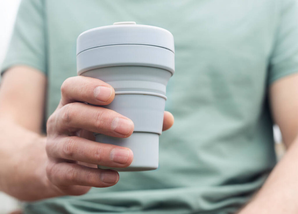 Collapsible cup for takeaway coffee or tea. Male hand with sustainable silicon mug. Modern people lifestyle - Foto, Imagen