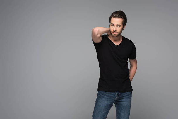 bearded man in black t-shirt and jeans standing isolated on grey - Photo, image