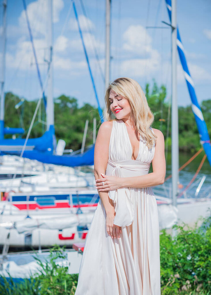 Nice blonde lady in yacht club. Woman in flying silk white dress at outdoor, relax time - Fotó, kép