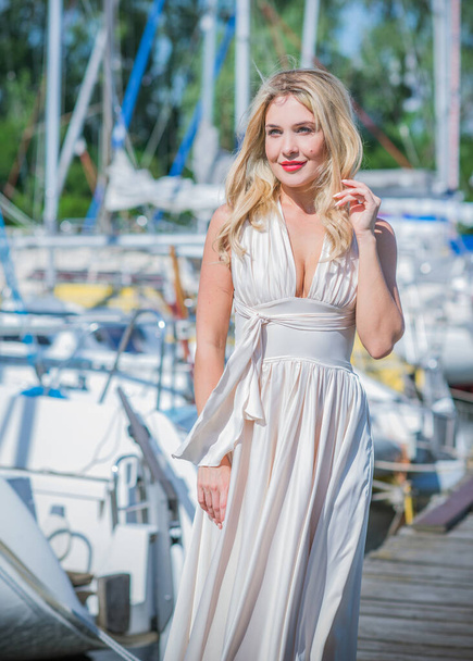 Nice blonde lady in yacht club. Woman in flying silk white dress at outdoor, relax time - Fotó, kép