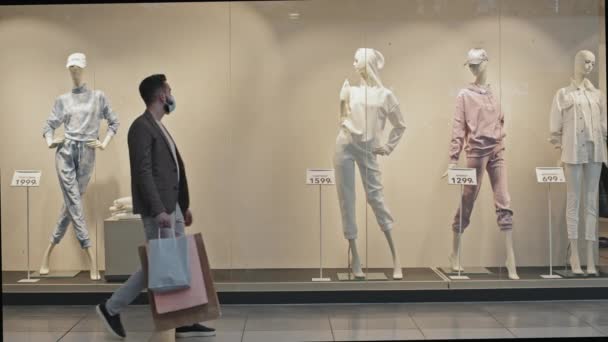 Teljes szúrás lövés elegáns jóképű férfi arc maszk elhaladó ablak kijelzők elegáns ruházati bolt előtt áll a próbababa, hogy képet készítsen a ruhát az okostelefon - Felvétel, videó