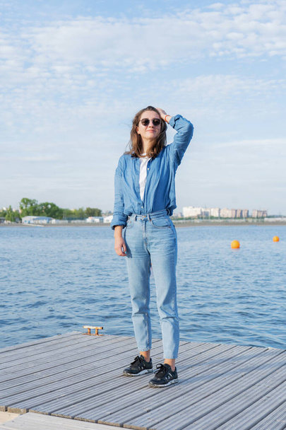 A young woman, fashionably dressed in an urban casual style, stands on a pontoon on a sunny spring day. - 写真・画像
