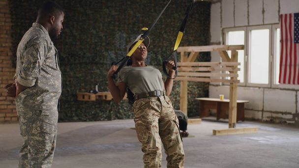 Schwarze Soldatin beim Training mit TRX Seilen in der Nähe des Trainers - Foto, Bild