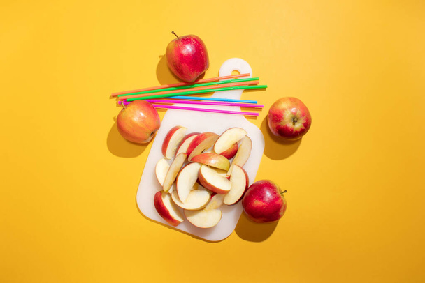 Chopped red apple on a board. Orange background and straws. Minimal concept. - Foto, imagen