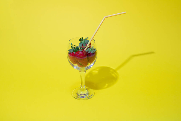 Glass with strawberries and straws on a yellow background. - Foto, afbeelding