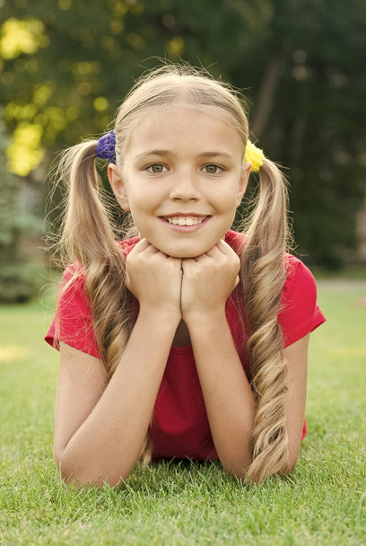 Little girl cute ponytails hairstyle relaxing on green grass, summer camp concept - Fotó, kép