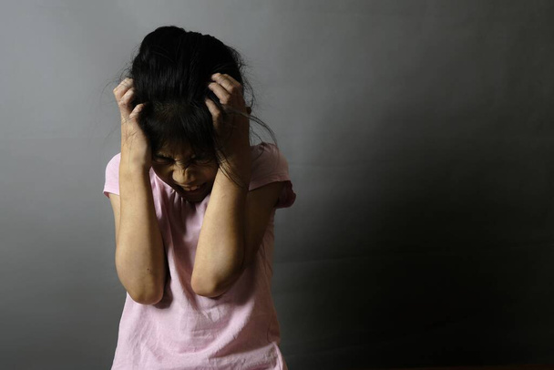 Konzept Kindesmissbrauch. Ein trauriges und verängstigtes Mädchen sitzt allein in einem dunklen Raum, die Hände bedecken ihren Kopf und fühlen sich einsam, gestresst und verängstigt.. - Foto, Bild