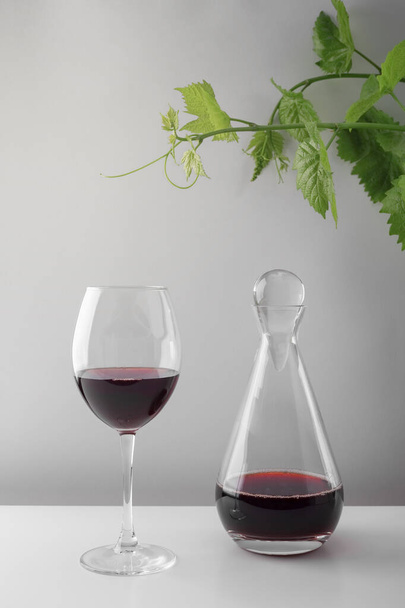 Een glas rode wijn en een karaf op een witte tafel. Lichte achtergrond. - Foto, afbeelding
