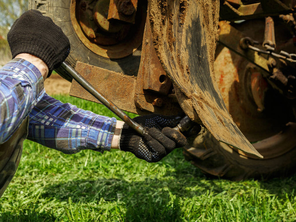 Man in black gloves repairs plough mounted on tractor. - Fotó, kép