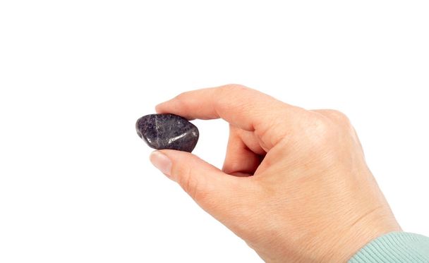 Woman holding purple color tumbled Iolite or Cordierite gemstone in hand, isolated on white background, lot of copy space. Also called "water-sapphire" and "Vikings' Compass", "steinheilite". - Photo, Image