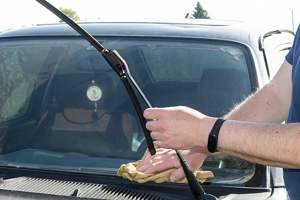 Mikrofiber bezle erkek elleri silecekleri tutarak arabanın ön camını siler..  - Fotoğraf, Görsel