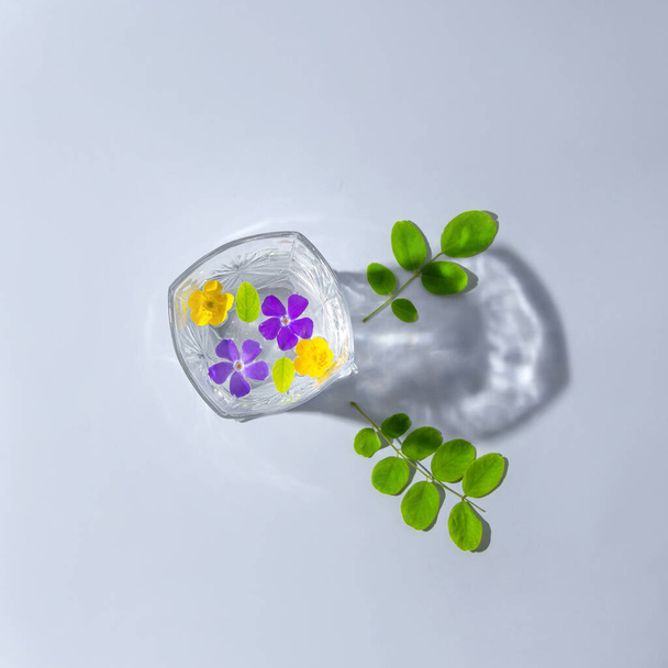 Jugo de flores. Flores en un vaso de agua. Sombra de un vaso. Sobre un fondo gris. Composición mínima. - Foto, imagen