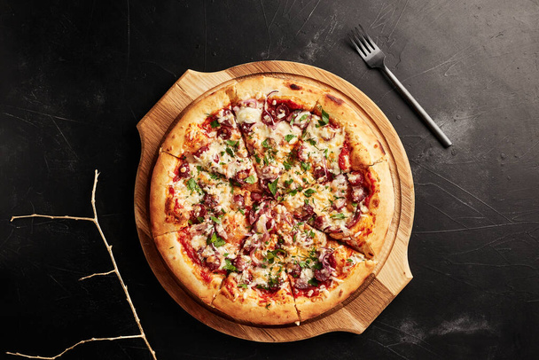 Pizza auf Holzsockel auf schwarzem strukturiertem Hintergrund von oben - Foto, Bild
