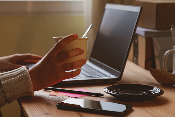 Fotografia della scrivania e delle mani di una giovane donna, che beve un caffè caldo o un'infusione, la mattina presto, mentre lavora a casa, a Madrid, Spagna. - Foto, immagini