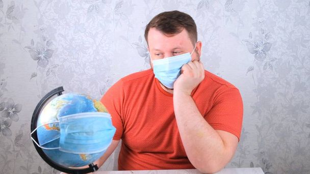 maschio sta guardando il globo con una maschera protettiva e un vaccino pandemico. Concetto di trattamento del virus Corona, iniezione, studi clinici durante una pandemia. Concetto di viaggio durante una pandemia - Foto, immagini