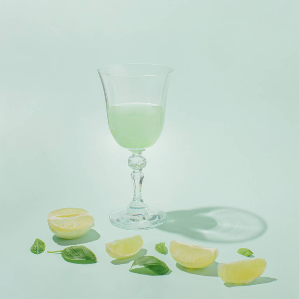 Retro summer idea, healthy food concept with drinking glass, peeled fresh raw lemon and herb leaves on pastel mint green background.. - Фото, зображення