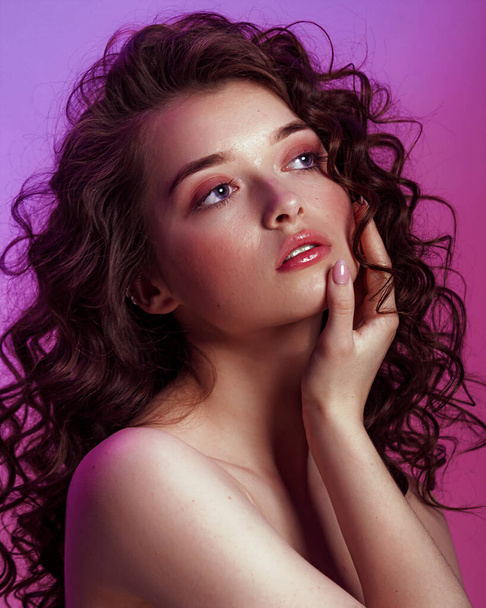 Brunette woman with long , shiny wavy hair . Beautiful face model with curly hairstyle . Woman with hands french manicure on pink neon background - Fotografie, Obrázek