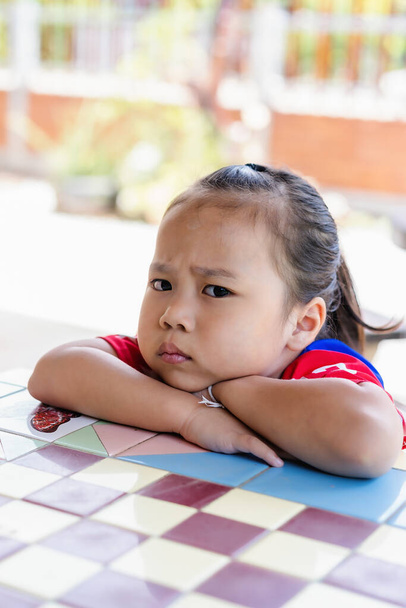 Angry little girl sitting and looking at camera. Unhappy child feeling upset and sad with a negative attitude. Depressed girl being disciplined pouting and looking sad. Sign and gesture emotional concept - Photo, Image