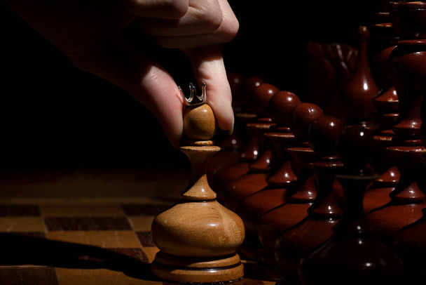 female hand holds a pawn with a crown on a dark background. old chess. business concept - Foto, afbeelding