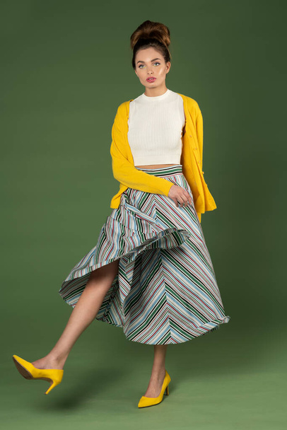 young woman taking a fashion pose on green background , she is very beautiful , wearing striped gown and yellow jacket , old style feeling and concept - Foto, afbeelding