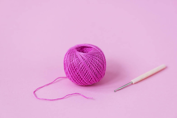 Pink skein of thread with a crochet hook on a pink background. - Foto, imagen
