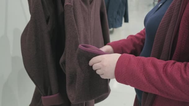 Беременная женщина выбирает шерстяную бордовую куртку с капюшоном в магазине, чтобы купить - Кадры, видео
