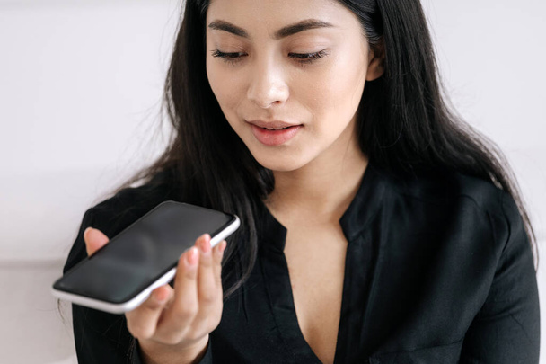 Online aplikace koncept. Mladá asijská podnikatelka nahrává hlasovou zprávu na smartphone pro kolegu nebo klienta. Usmívající se žena používající reproduktor na mobilním telefonu s makupem displej, zavřít portrét - Fotografie, Obrázek