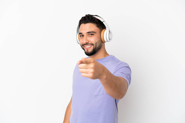 Молодий арабський чоловік ізольований на білому тлі слухаючи музику і вказуючи на фронт
 - Фото, зображення