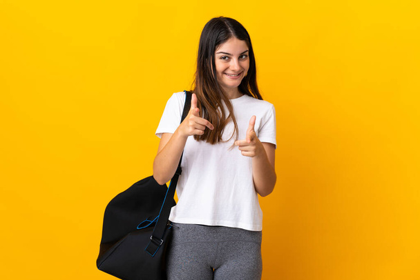 Young sport woman with sport bag isolated on yellow background pointing to the front and smiling - Valokuva, kuva