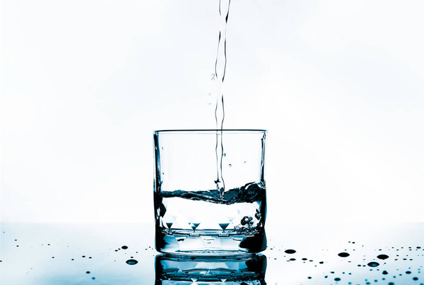Verter agua potable purificada y burbujas en vidrio transparente y gotas en el piso de selección.  - Foto, imagen