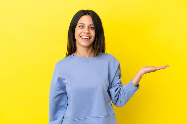 Young caucasian woman isolated on yellow background holding copyspace imaginary on the palm to insert an ad - Foto, immagini