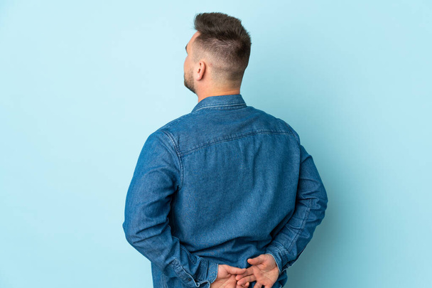Russian handsome man isolated on blue background in back position and looking back - Fotó, kép