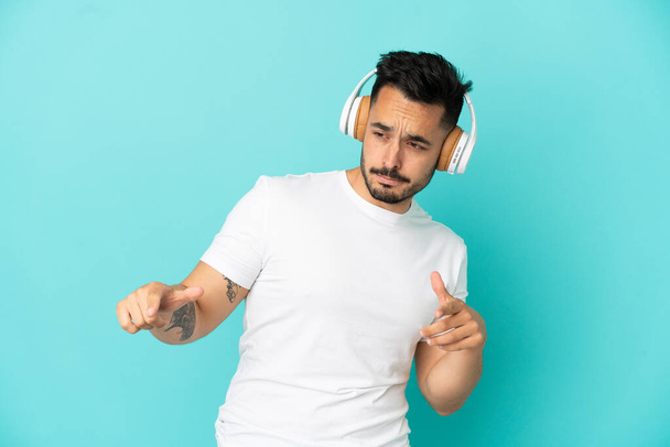 Young caucasian man isolated on blue background listening music and dancing - Foto, afbeelding