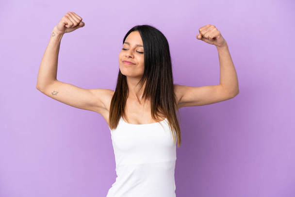 Young caucasian woman isolated on purple background doing strong gesture - Photo, Image