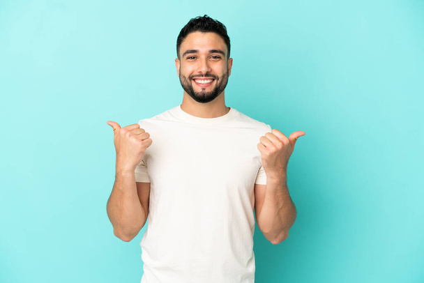 Young arab man isolated on blue background with thumbs up gesture and smiling - Foto, Imagem