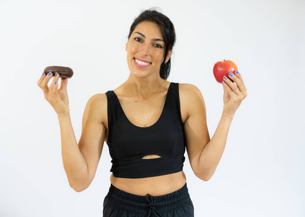 Young hispanic woman holding apple and donuts smiling with a happy and cool smile on face. showing teeth. - Φωτογραφία, εικόνα