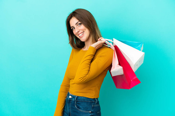 Beyaz kadın mavi arka planda izole edilmiş alışveriş torbaları tutuyor ve gülümsüyor. - Fotoğraf, Görsel
