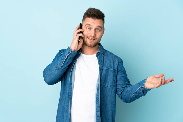 Russian handsome man isolated on blue background keeping a conversation with the mobile phone with someone - Фото, зображення